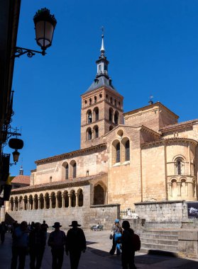 The statue of Juan Bravo stands before the Romanesque Church of San Martn in Segovia. The historic landmark, featuring a tall tower, is beautifully framed against a clear blue sky.