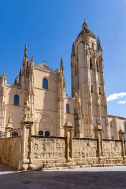 Segovia's massive Cathedral of Santa Mara dominates the plaza. Its Gothic style towers over the bustling public space, where Segovian life unfolds under a blue sky