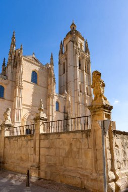 Segovia's massive Cathedral of Santa Mara dominates the plaza. Its Gothic style towers over the bustling public space, where Segovian life unfolds under a blue sky