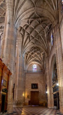 The Segovia Cathedral interior showcases towering Gothic arches and an ornate vaulted ceiling. Massive columns frame the central altarpiece and detailed stained glass