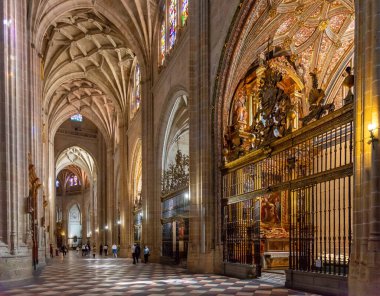 The Segovia Cathedral interior showcases towering Gothic arches and an ornate vaulted ceiling. Massive columns frame the central altarpiece and detailed stained glass