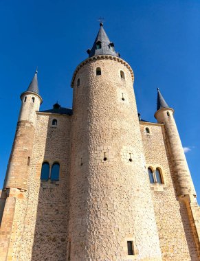 Alczar 'ın en yüksek kulesinin dramatik ve alçak açılı görüntüsü. Ana kulede eşsiz desenli bir taş ve yoğun mavi gökyüzüne karşı dik konik bir çatı var.