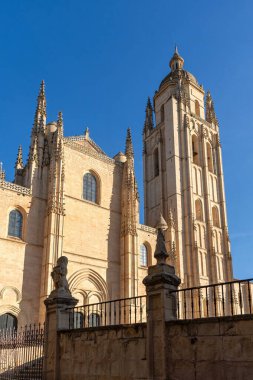 Segovia Katedrali 'nin çan kulesinin ve yan cephesinin dramatik, günbatımına yakın, günbatımına yakın Gotik taş işçiliği ve düşük koruma duvarı sergileniyor.