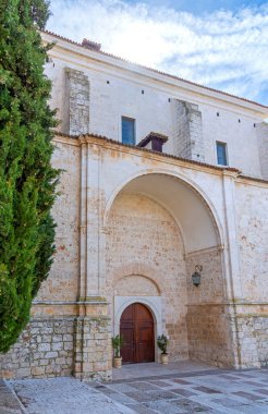 İspanya 'nın Chinchn kentindeki Meryem Ana Kilisesi' nin heybetli beyaz taş cephesinde selvi ağaçları, kemerli bir giriş ve taş bir haç yer alıyor.