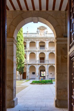 Alcal de Henares - İspanya - 9 Nisan 2025: Alcal Üniversitesi 'nin Rönesans avlusu taş bir kapı eşiği tarafından çerçevelenmiştir. Üç kemerli galeri katları, uzun bir selvi ağacı ve küçük bir merkez bahçe.