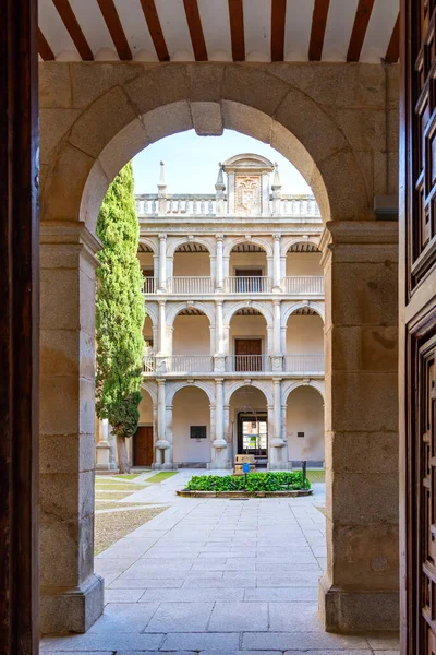 Alcal de Henares - İspanya - 9 Nisan 2025: Alcal Üniversitesi 'nin Rönesans avlusu taş bir kapı eşiği tarafından çerçevelenmiştir. Üç kemerli galeri katları, uzun bir selvi ağacı ve küçük bir merkez bahçe.