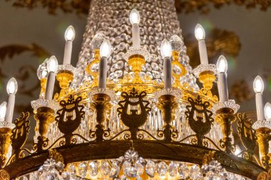 El Pardo Sarayı 'ndaki görkemli kristal ve altın avizenin yakın plan bir ayrıntısı. Çok sayıda elektrikli mum ışığı ve lire motifli pirinç metal işçiliğinin yer aldığı bir yer.