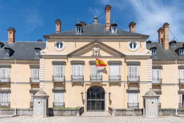 El Pardo Kraliyet Sarayı 'nın klasik cephesi, mermer duvarları, dik tahta çatıları, köşe kulesi ve parlak mavi gökyüzünün altındaki bitişik şapel yapısı.