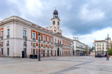 Madrid 'in Puerta del Sol kentindeki tarihi Real Casa de Correos' ta, ikonik saat kulesi, kırmızı tuğla ve beyaz taş cephe ve merkez balkondan dalgalanan İspanyol ve AB bayrakları yer alıyor.