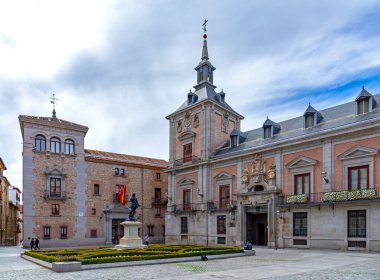 Madrid 'in tarihi Plaza de la Villa' sı, Ivaro de Bazn heykelinin yanındaki kırmızı tuğla kulesiyle eski Casa de la Villa 'yı ve desenli bahçe çitlerini sergiliyor.