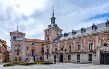 Madrid 'in tarihi Plaza de la Villa' sı, Ivaro de Bazn heykelinin yanındaki kırmızı tuğla kulesiyle eski Casa de la Villa 'yı ve desenli bahçe çitlerini sergiliyor.