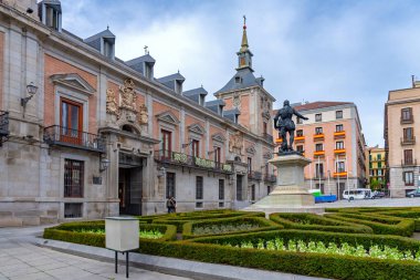 Madrid 'in tarihi Plaza de la Villa' sı, Ivaro de Bazn heykelinin yanındaki kırmızı tuğla kulesiyle eski Casa de la Villa 'yı ve desenli bahçe çitlerini sergiliyor.