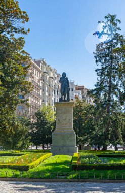 The bronze statue of painter Francisco de Goya on a stone pedestal, set in a formal garden with hedges and trees, near the entrance to the Museo del Prado in Madrid