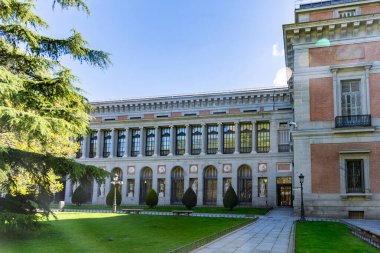El Prado Museum on a sunny spring morning, showcasing elegant neoclassical architecture, grand statues, and lush green trees framing its bright, inviting faade with added charm