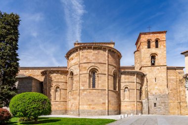Manikürlü yeşil çalıların ve parlak mavi gökyüzünün altındaki yüksek ağaçların arkasında, San Pedro 'nun sıcak altın taştan yapılma Vilas Kilisesi' nin Romen maymunu ve çan kulesi yükselir.