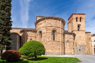 Manikürlü yeşil çalıların ve parlak mavi gökyüzünün altındaki yüksek ağaçların arkasında, San Pedro 'nun sıcak altın taştan yapılma Vilas Kilisesi' nin Romen maymunu ve çan kulesi yükselir.