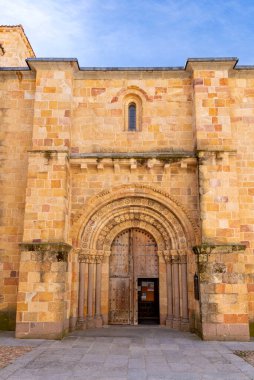 San Pedro Kilisesi 'nin Roma portalına yakın plan, küçük bir pencerenin altında yuvarlak oymalı kemer, taş sütunlar ve yıpranmış ahşap çift kapılar gösteriliyor.