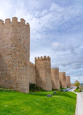 Vilas antik taş duvarlar, yüksek yuvarlak kuleler, parlak yeşil bir set üzerinde yükseliyor ve yumuşak bulutlu bir gökyüzü altında yerleşir