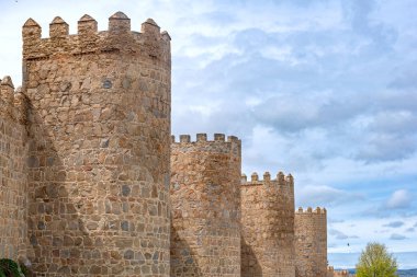 Vilas antik taş duvarlar, yüksek yuvarlak kuleler, parlak yeşil bir set üzerinde yükseliyor ve yumuşak bulutlu bir gökyüzü altında yerleşir