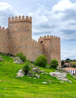 Vilas antik taş duvarlar, yüksek yuvarlak kuleler, parlak yeşil bir set üzerinde yükseliyor ve yumuşak bulutlu bir gökyüzü altında yerleşir