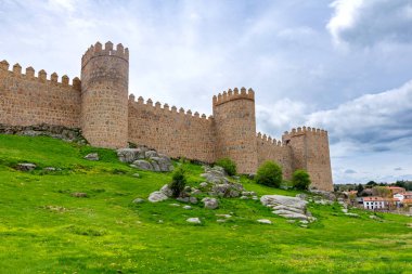 Vilas antik taş duvarlar, yüksek yuvarlak kuleler, parlak yeşil bir set üzerinde yükseliyor ve yumuşak bulutlu bir gökyüzü altında yerleşir