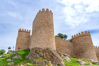 Vilas antik taş duvarlar, yüksek yuvarlak kuleler, parlak yeşil bir set üzerinde yükseliyor ve yumuşak bulutlu bir gökyüzü altında yerleşir