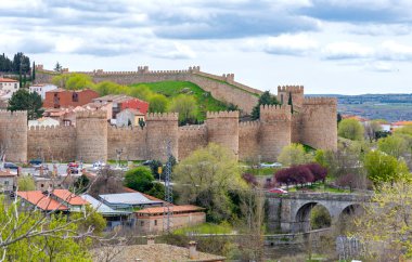 Panoramik katmanlı vila duvarları, taş kuleler ve çentikli surlar kemerli taş bir köprünün üzerindeki yeşil bir tepeden yükselen çentikli duvarlar ve modern şehirler seramik çatılar