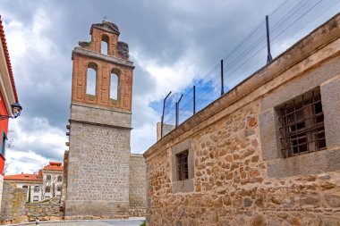 Leylek yuvası olan kırmızı tuğlalı bir çan kulesinin dramatik manzarası ve dar bir kaldırım taşından geçidin üzerinde yükselen kemerli açıkları. Villasında parmaklıklı penceresi olan alçak bir taş binanın yanında.