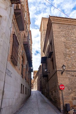 Toledo 'da dar taştan sokaklar demir balkonlu yüksek binalar, tahta pencere panjurları ve fenerler arasında esiyor, zamansız, eski şehir atmosferi yaratıyor.