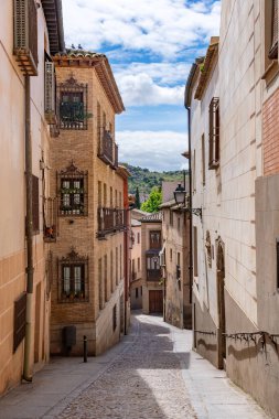 Toledo 'da dar taştan sokaklar demir balkonlu yüksek binalar, tahta pencere panjurları ve fenerler arasında esiyor, zamansız, eski şehir atmosferi yaratıyor.