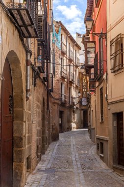 Toledo 'da dar taştan sokaklar demir balkonlu yüksek binalar, tahta pencere panjurları ve fenerler arasında esiyor, zamansız, eski şehir atmosferi yaratıyor.