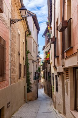 Toledo 'da dar taştan sokaklar demir balkonlu yüksek binalar, tahta pencere panjurları ve fenerler arasında esiyor, zamansız, eski şehir atmosferi yaratıyor.