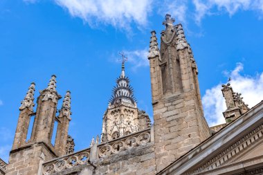 Gökyüzünde yükselen Gotik taş duvarları, süslü kemerleri, zirveleri ve heykel detaylarını gösteren Toledo Katedrali 'nin yukarı dış görünüşü