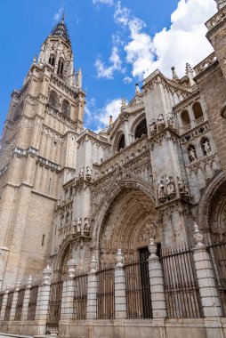 Gökyüzünde yükselen Gotik taş duvarları, süslü kemerleri, zirveleri ve heykel detaylarını gösteren Toledo Katedrali 'nin yukarı dış görünüşü