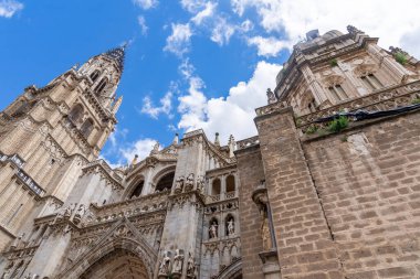 Gökyüzünde yükselen Gotik taş duvarları, süslü kemerleri, zirveleri ve heykel detaylarını gösteren Toledo Katedrali 'nin yukarı dış görünüşü