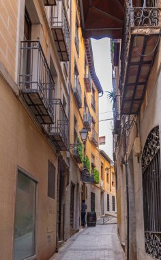 Dar bir kaldırım taşı Toledo caddesinin aşağı dikey görüntüsü, sıcak sıva cepheleri, dövmeli demir balkonlar, açıkta taş ve uzak bir ahşap balkon ile kaplı