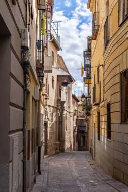 Dar bir kaldırım taşı Toledo caddesinin aşağı dikey görüntüsü, sıcak sıva cepheleri, dövmeli demir balkonlar, açıkta taş ve uzak bir ahşap balkon ile kaplı