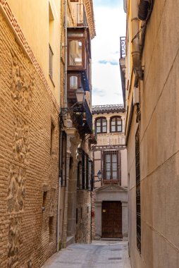Dar bir kaldırım taşı Toledo caddesinin aşağı dikey görüntüsü, sıcak sıva cepheleri, dövmeli demir balkonlar, açıkta taş ve uzak bir ahşap balkon ile kaplı