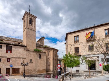 Toledo 'daki Iglesia de San Vicente' nin dikey görüntüsü, Mudjar tuğla kulesini vurguluyor ve kör kemerlerle çevrili, yumuşak bulutlu mavi gökyüzüne karşı dizilmiş.
