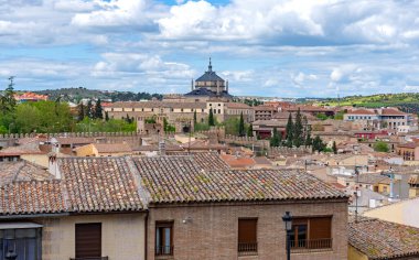 Toledo çatıları ve tarihi şehir duvarları boyunca, Büyük Hastane de Tavera ve arka planda yükselen tahta kubbesi ile bulutlu mavi gökyüzünün altında