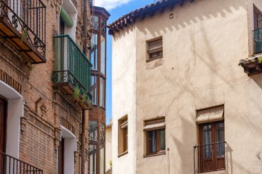 Toledo 'da tuğla ve sıva cepheli geleneksel binalar, dövmeli demir balkonlar ve mavi gökyüzünün altındaki dar bir caddede uzun cam bir mirador.