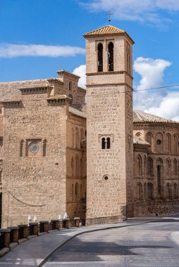 Toledo 'daki Mudjar stili Santiago del Arrabal kilisesinin dikey görüntüsü, uzun taş çan kulesi ve parlak bulutlu gökyüzünün altında tuğla kemerli maymunu barındırıyor.