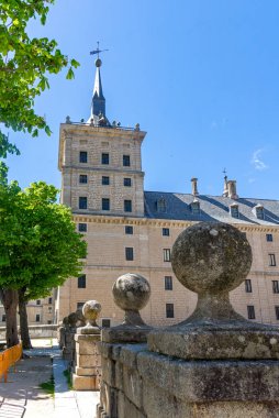 Granit bir duvardaki dekoratif taş küreler açık güneşli bir günde İspanya 'nın San Lorenzo kentindeki El Escorial Manastırı' nın köşe kulesinin ve kayrak çatısının manzarasını oluşturuyor.