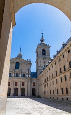 İspanya 'daki El Escorial' da güneşli bir iç avlu, devasa granit kuleler, tek cepheli cepheler ve büyük bir bazilika girişi. San Lorenzo