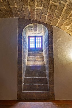 Güneş ışığıyla aydınlatılmış taş bir merdiven ve ağır granit kemerler, El Escorial 'ın içindeki kraliyet panteonlarına doğru uzanır.