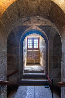 Güneş ışığıyla aydınlatılmış taş bir merdiven ve ağır granit kemerler, El Escorial 'ın içindeki kraliyet panteonlarına doğru uzanır.