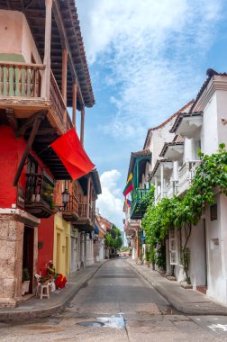 Cartagena, Kolombiya 'daki dar sömürge caddelerinde canlı renkli binalar, ikonik ahşap balkonlar ve parlak bir tropikal gökyüzü altında yemyeşil alanlar var.