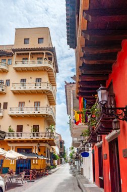 Cartagena, Kolombiya 'daki dar sömürge caddelerinde canlı renkli binalar, ikonik ahşap balkonlar ve parlak bir tropikal gökyüzü altında yemyeşil alanlar var.