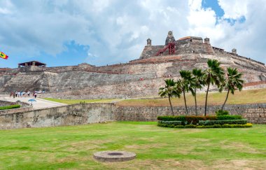San Felipe de Barajas Kalesi 'nin devasa taş duvarları, Kolombiya' nın başkenti Cartagena 'da bulutlu bir gökyüzünün altında yeşil çimlerin ve palmiye ağaçlarının üzerinde yükselir.