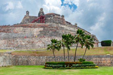 San Felipe de Barajas Kalesi 'nin devasa taş duvarları, Kolombiya' nın başkenti Cartagena 'da bulutlu bir gökyüzünün altında yeşil çimlerin ve palmiye ağaçlarının üzerinde yükselir.